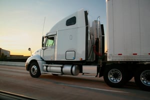 white tractor trailer driving down the road at dusk 