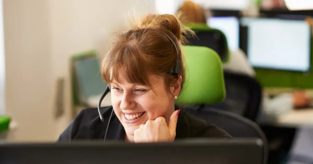 Smiling woman wearing headset at desk.